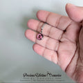 Hand holding a necklace with a pink heart pendant against a plain background