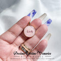 Hand holding a breastmilk and DNA keepsake necklace with 'Wendy' engraved, against a white background.