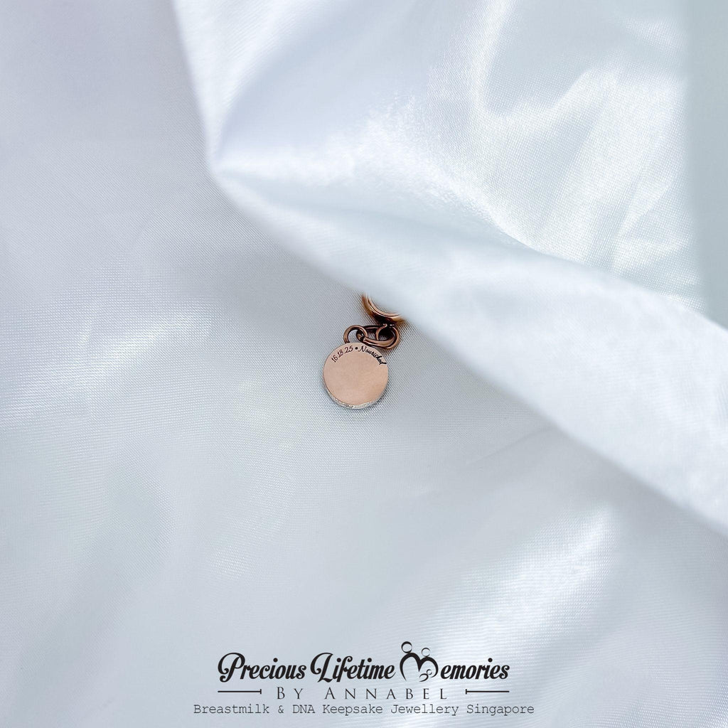 Rose gold charm on white fabric with 'Precious Lifetime Memories by Annabel' branding.