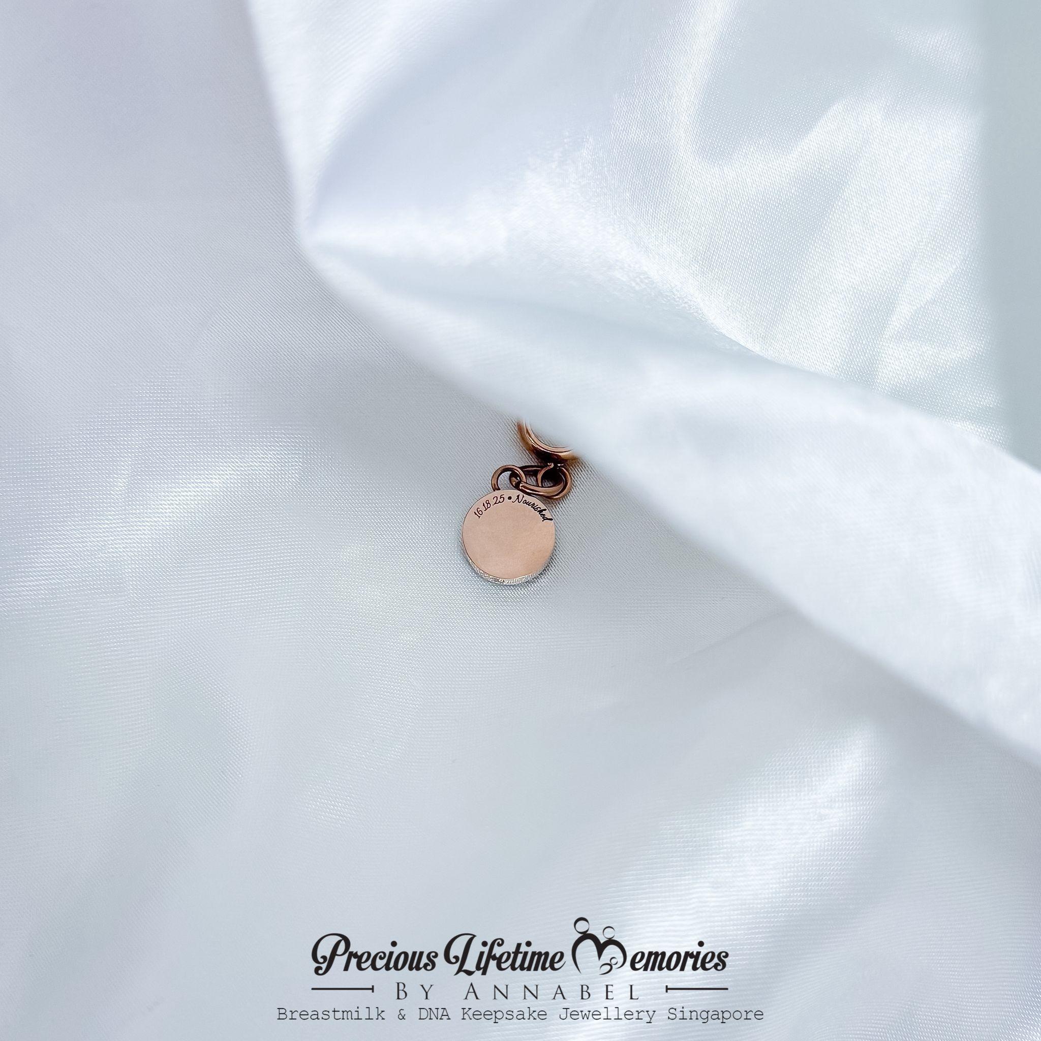 Rose gold charm on white fabric with 'Precious Lifetime Memories by Annabel' branding.